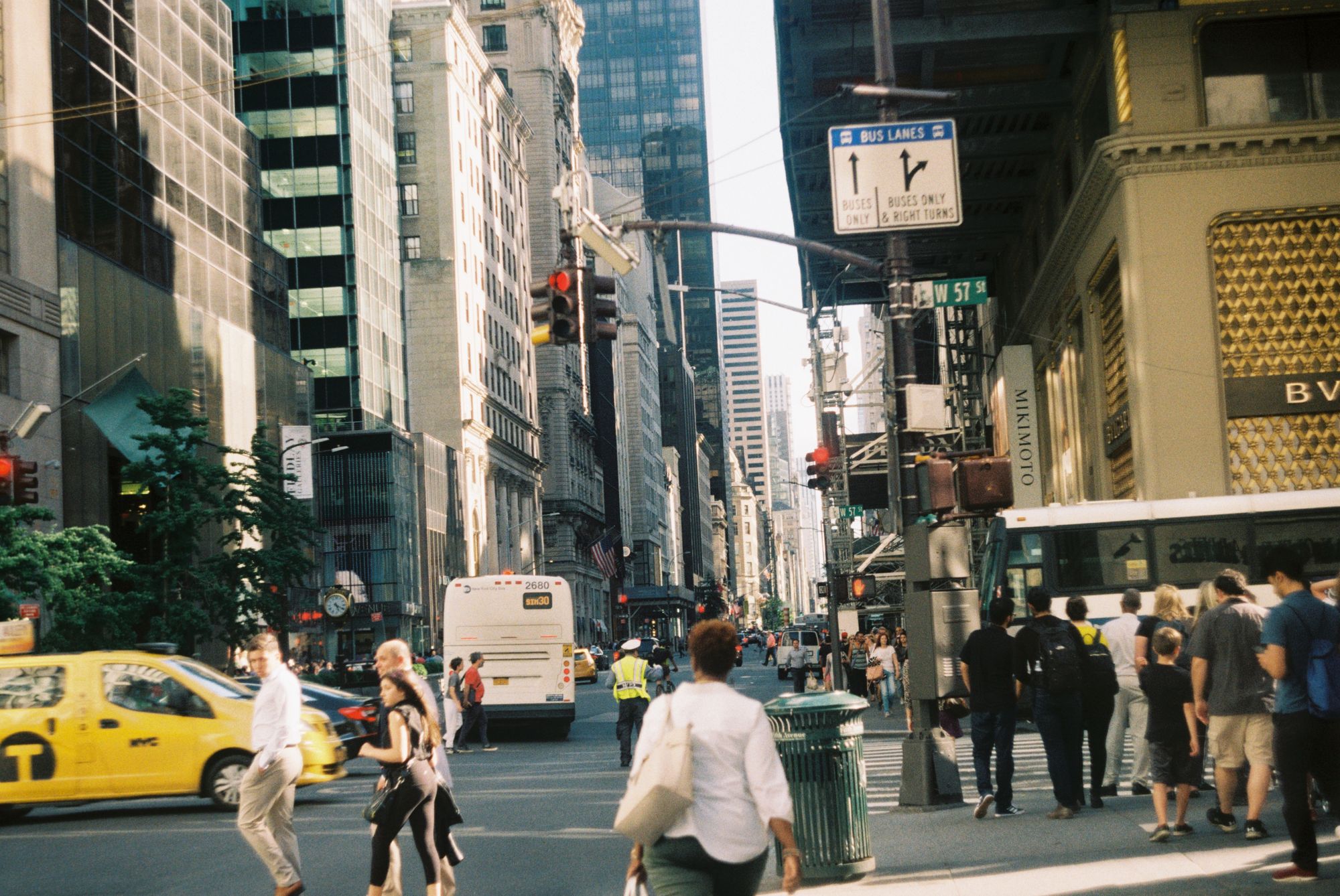 Menschen überqueren eine New Yorker Straße neben Bussen und Taxis